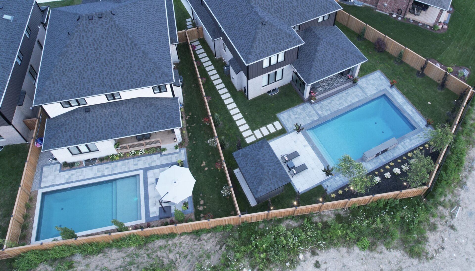 An overhead shot of two backyards with pools, surrounding plants, and wooden fences.